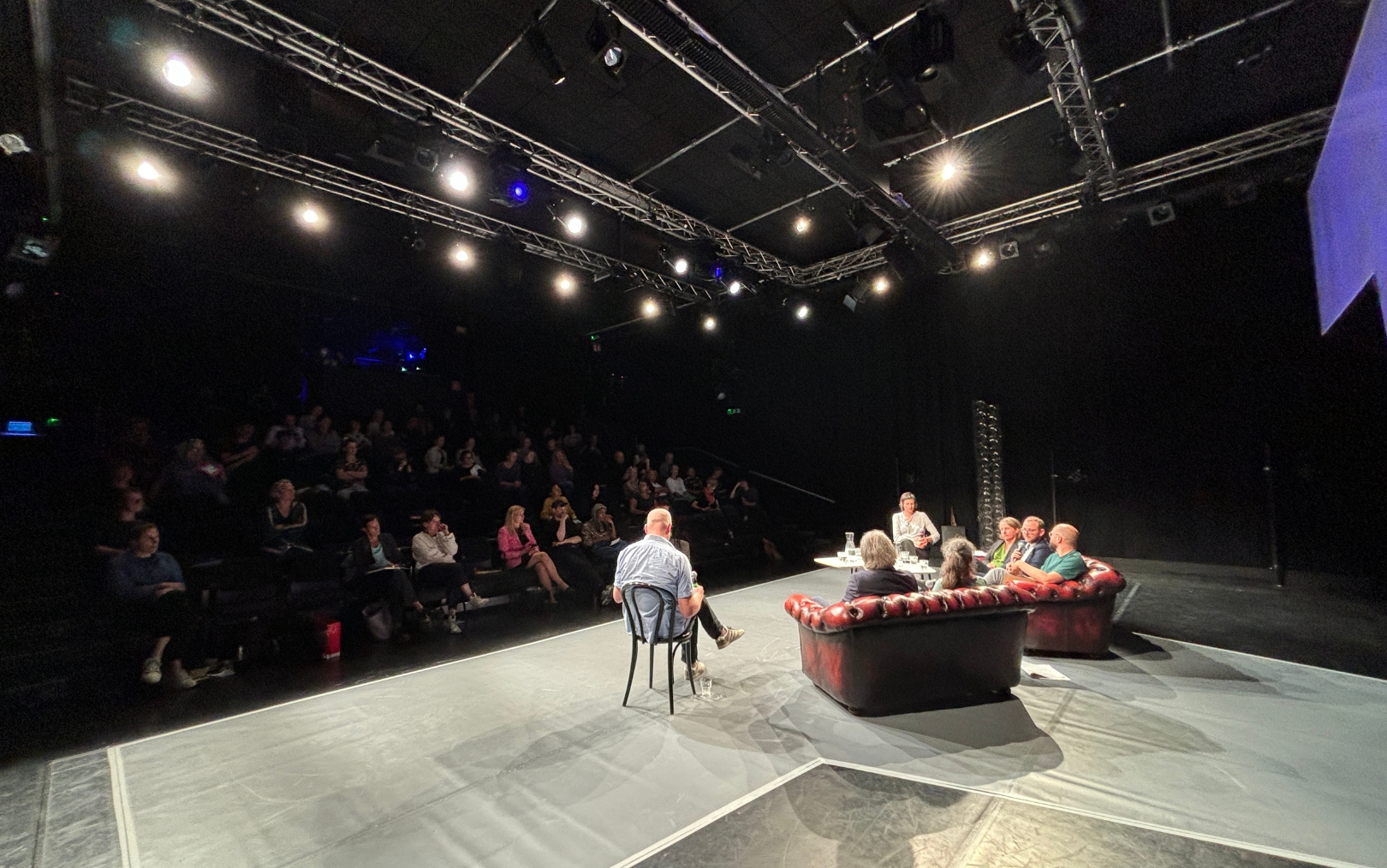 Podiumsdiskussion auf Bühne, Publikum im Dunkeln.