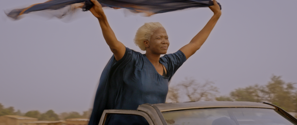 Frau in blauem Kleid steht freudig im Autodach, hält Tuch über dem Kopf.