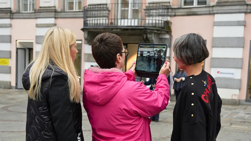 Drei Frauen, eine hält ein Tablet, stehen vor einem historischen Gebäude.