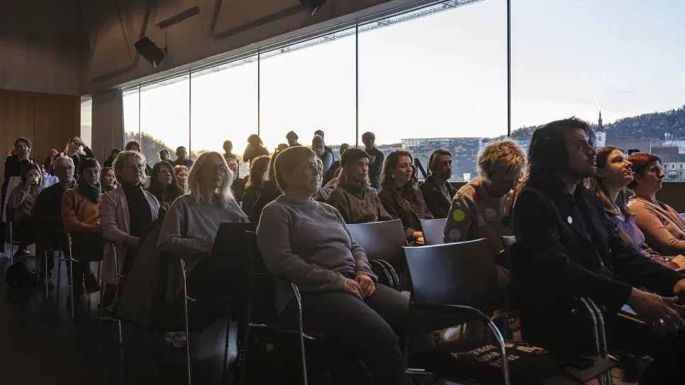 Publikum sitzt aufmerksam bei Tageslicht in einem modernen Konferenzraum.
