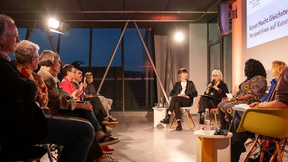 Podiumsdiskussion bei Abendlicht mit mehreren Frauen auf der Bühne und Publikum.