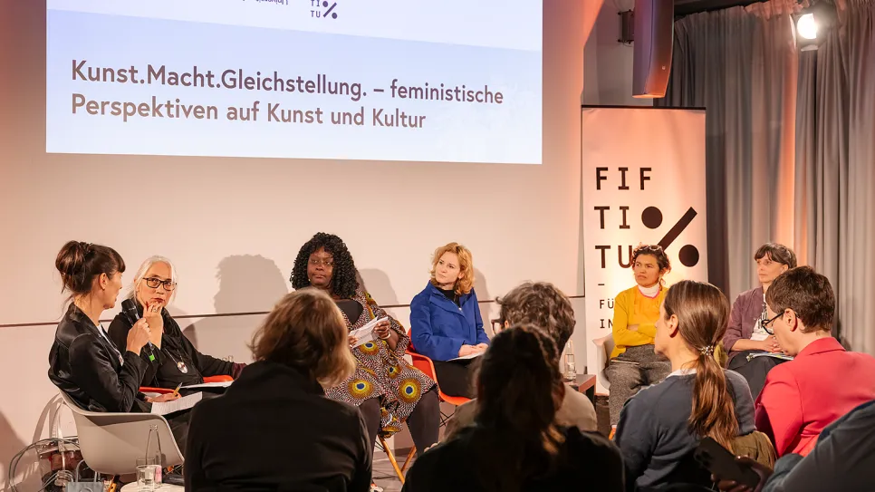 Podiumsdiskussion mit mehreren Teilnehmerinnen, Banner mit dem Thema feministische Perspektiven.