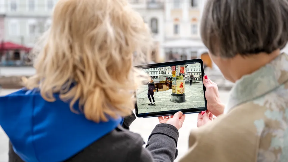 Zwei Frauen betrachten ein Foto auf einem Tablet im Freien.
