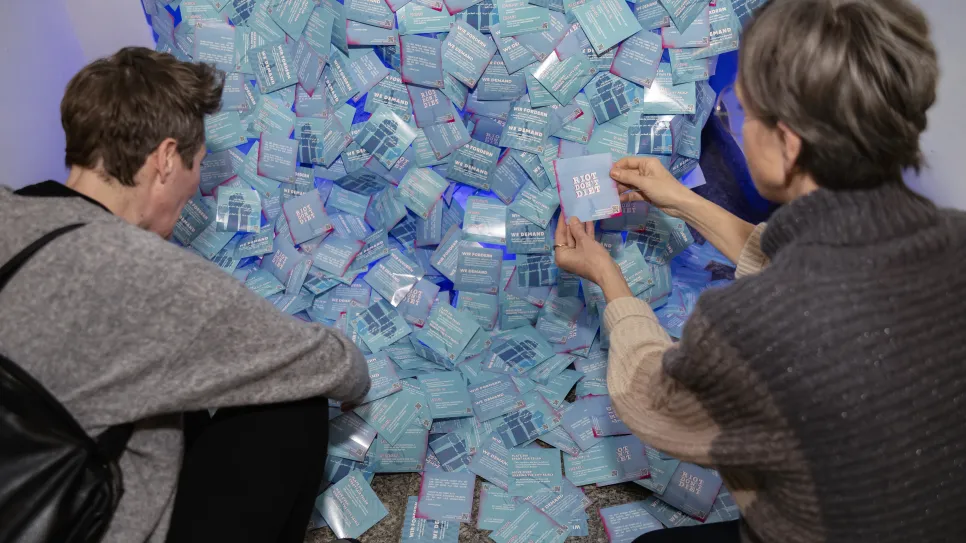 Zwei Personen untersuchen zahlreiche blaue Umschläge auf dem Boden.