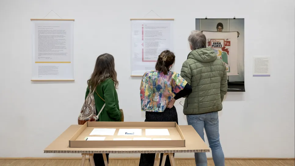 Drei Personen betrachten ausgestellte feministische Kunst in einer Galerie.