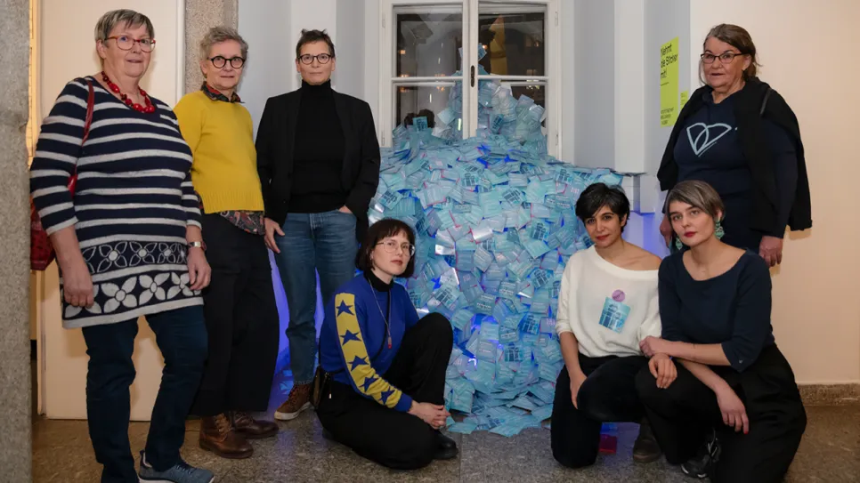 Frauen vor einer Installation aus blauen Plastikflaschen, posieren lächelnd in Galerie.