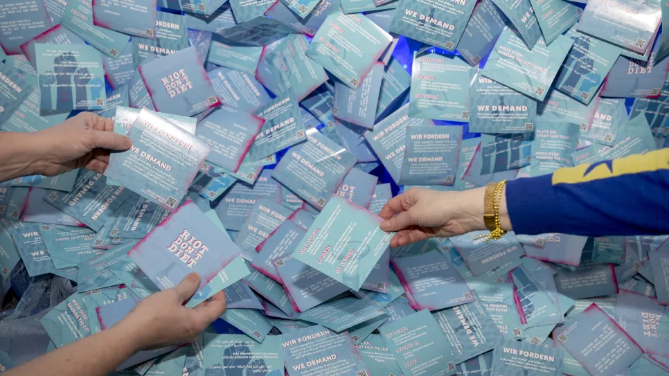 Viele blaue Flyer mit feministischen Botschaften, zwei Hände greifen jeweils einen Flyer.