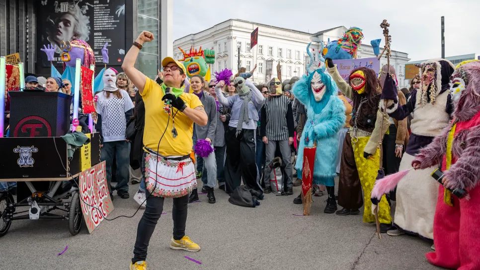 Demonstration mit verkleideten Menschen, bunte Kostüme, führende Person in gelb.