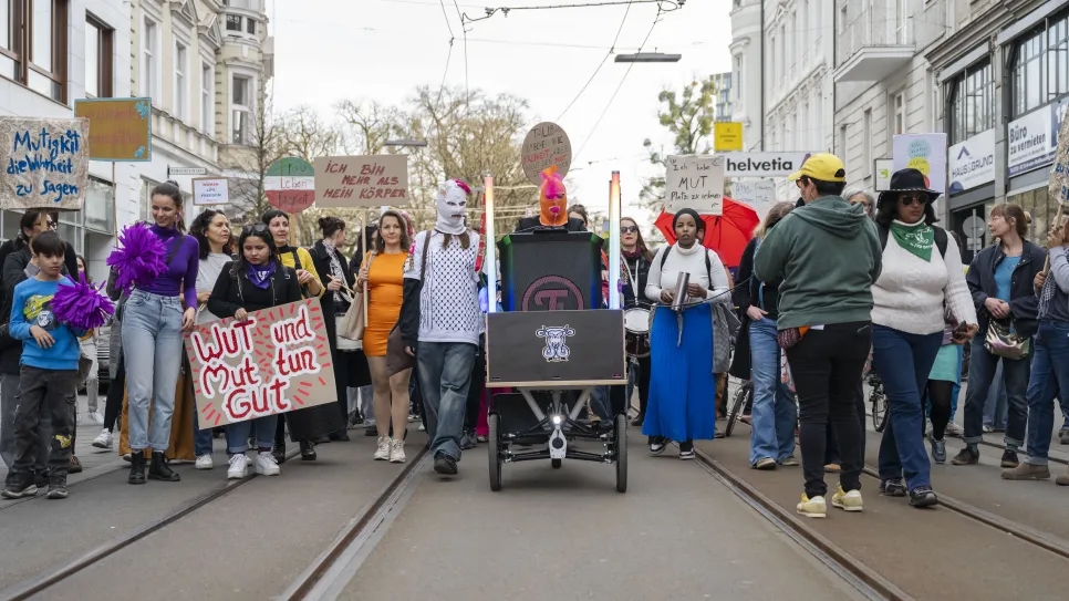 Demonstration von Aktivist*innen mit bunten Schildern auf einer Stadtstraße.
