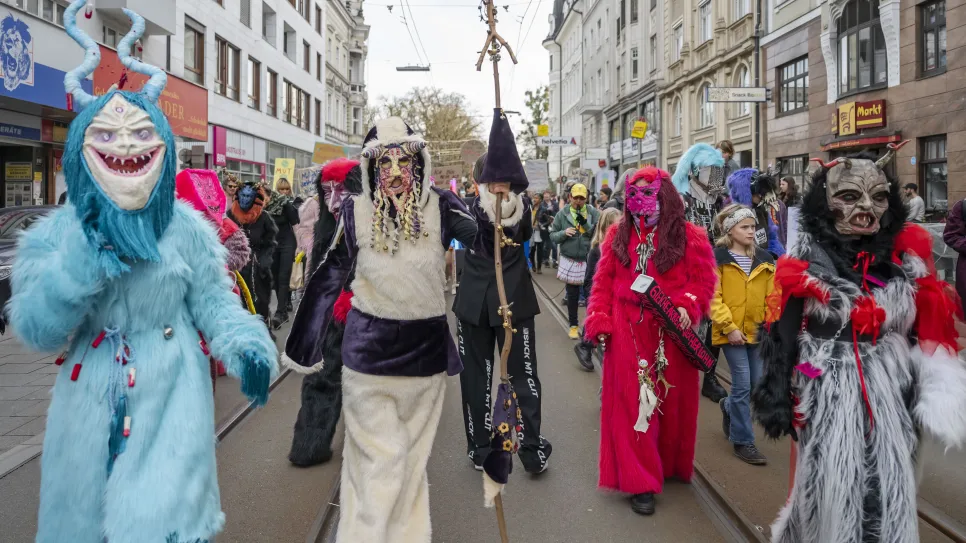 Menschen in bunten Kostümen und Masken bei einem Straßenumzug.