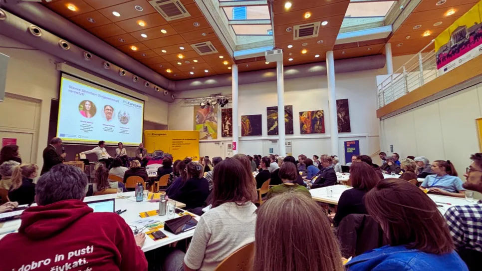 Teilnehmer in einem Konferenzraum, blicken auf eine Präsentation.