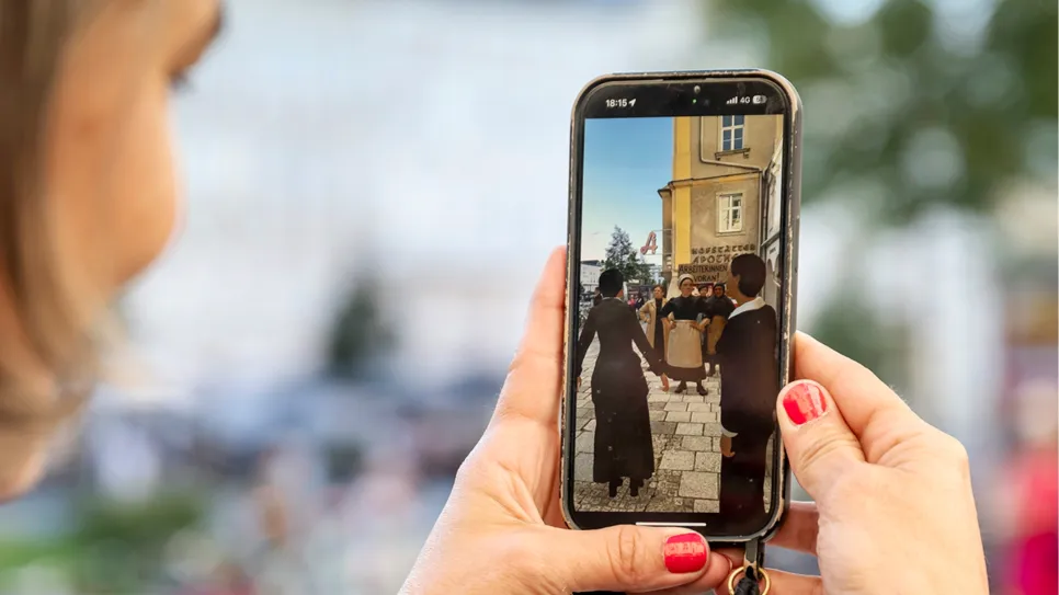 Frau hält Smartphone, zeigt Bild von Frauen beim Protest in der Stadt.