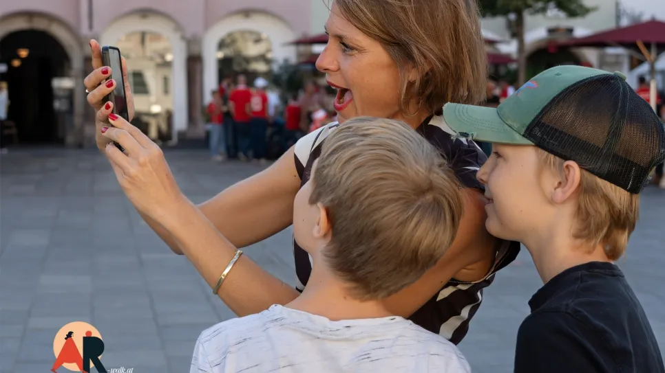 Frau mit zwei Kindern, fasziniert vom Smartphone auf belebtem Platz.