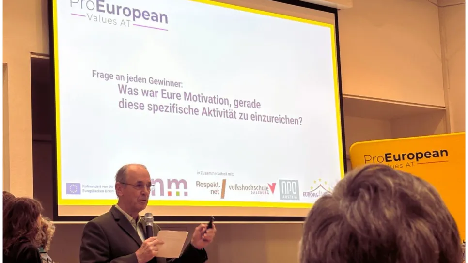 Mann spricht vor Publikum, Präsentation mit Pro European Logo im Hintergrund.