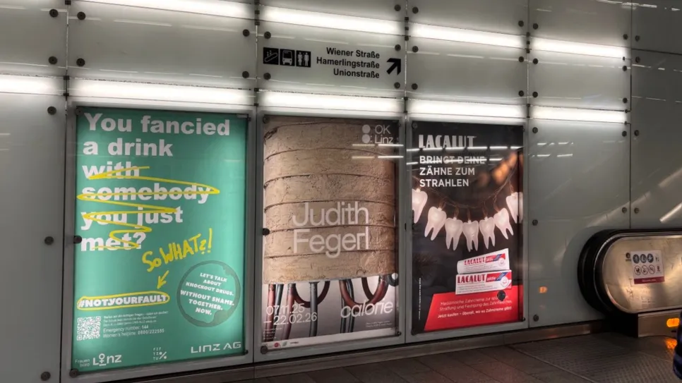 Drei beleuchtete Plakate in einer U-Bahn-Station, Eskalator rechts.