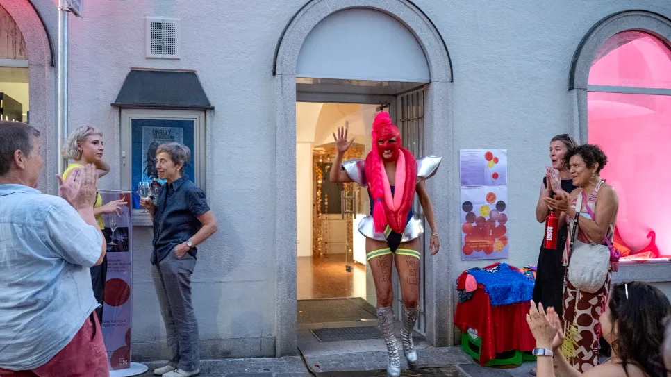Person in auffälligem Kostüm bei Veranstaltung, umgeben von applaudierenden Menschen.