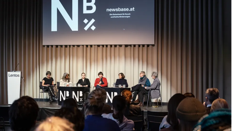 Podiumsdiskussion mit sieben Personen, Logo „Nb“ im Hintergrund.