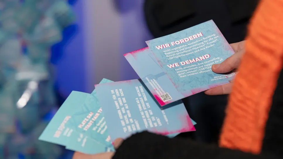 Person hält Flyer mit feministischen Forderungen in Blau und Pink.
