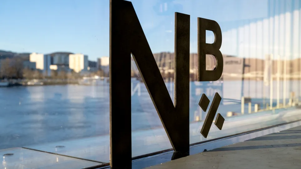 Logo „N×B“ auf Glaswand mit Fluss und Stadt im Hintergrund.