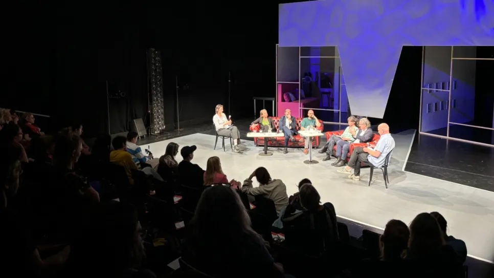 Podiumsdiskussion mit sieben Personen auf einer Bühne, Publikum im Vordergrund.
