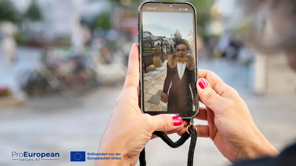 Person hält Smartphone mit Selfie-Kamera, Fokus auf Bildschirm, draußen. ProEuropean Logo sichtbar.