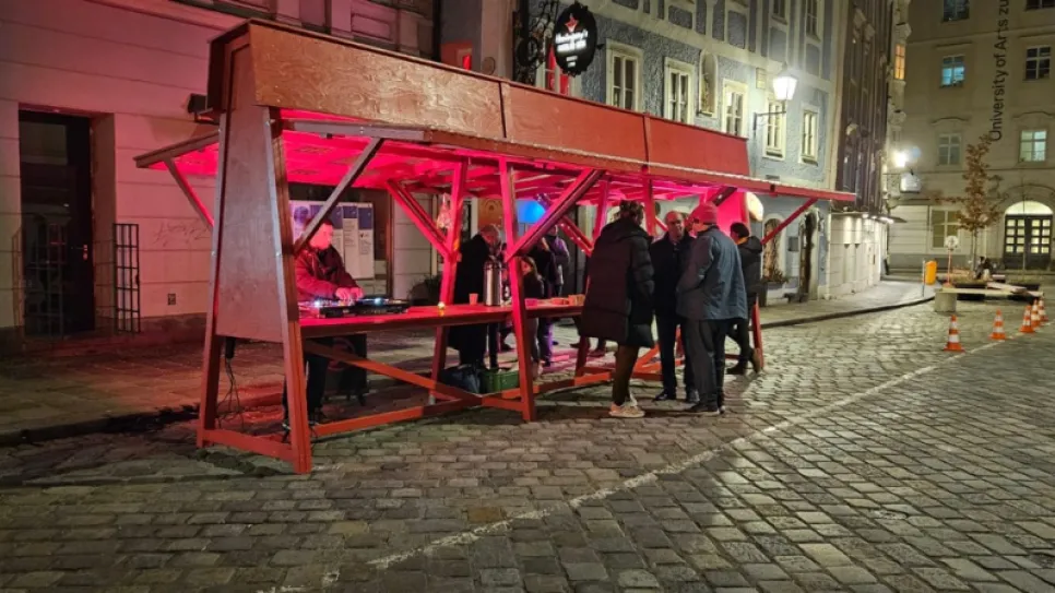 Roter Straßenstand bei Nacht, umgeben von Menschen, urbane Umgebung.
