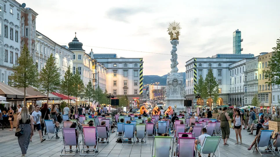 Menschenmenge auf Stadtplatz mit bunter Bestuhlung, Livemusik im Hintergrund.