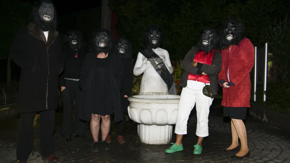 Gruppenkostüm mit Gorilla-Masken um Statue bei Nacht.