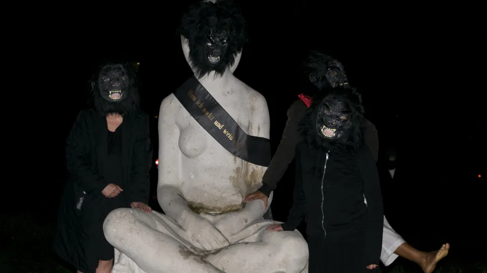 Vier Personen mit Gorilla-Masken stehen um eine große Skulptur.