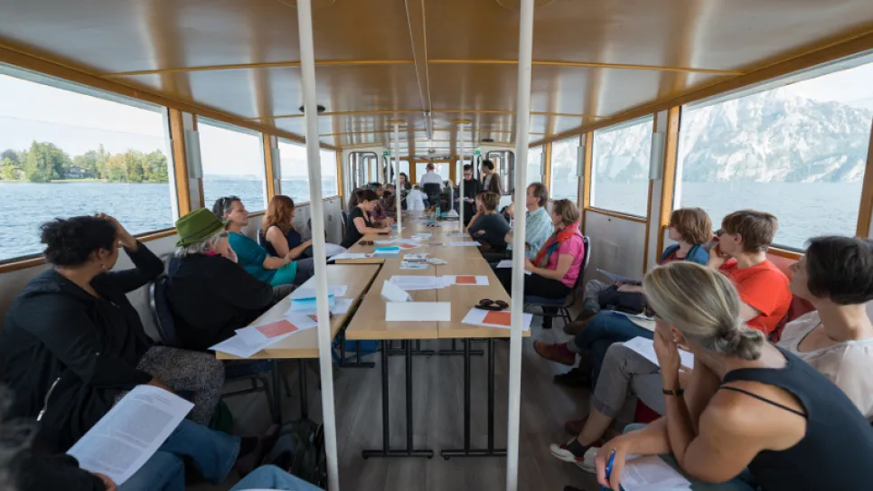 Frauen diskutieren in einer Bootskabine, Seeblick im Hintergrund.