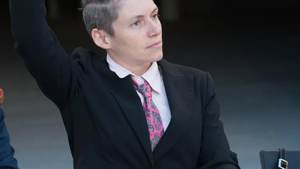 Person in Anzug hebt Hand bei Konferenz.