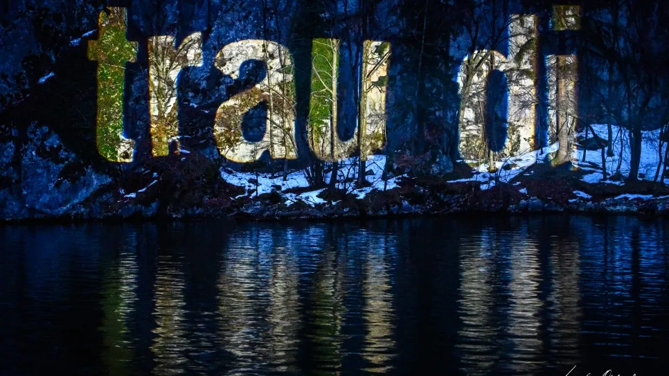 Leuchtende Buchstaben "trau di" über einem Gewässer bei Nacht.
