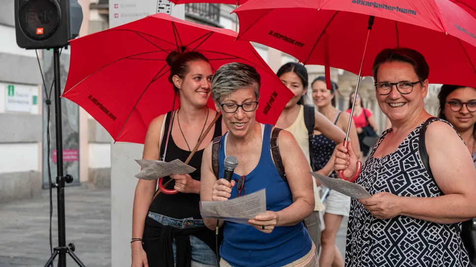 Frauen mit roten Regenschirmen lächeln und lesen in einer Stadt, sommerliche Kleidung.