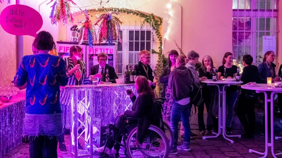 Menschen bei einer feministisch dekorierten Veranstaltung, lila Beleuchtung.