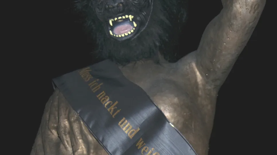Skulptur einer Person mit Gorilla-Maske und Schärpe.