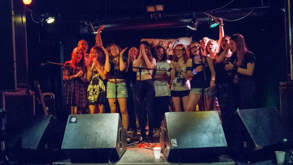 Frauen auf Bühne, lächeln und feiern, in einem Club mit dunkler Beleuchtung. Fotografiert.
