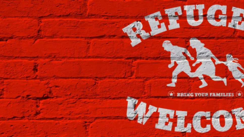 Rote Ziegelwand mit Grafik einer Flüchtlingsfamilie und Text "Refugees Welcome".