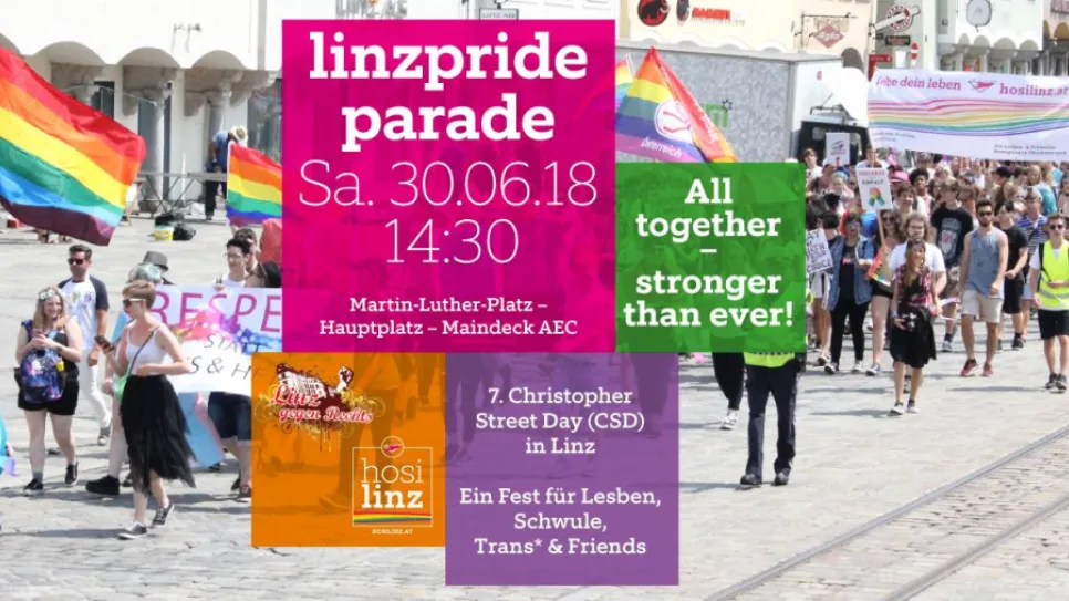 Menschen bei einer Parade mit Regenbogenfahnen auf einer sonnigen Straße.