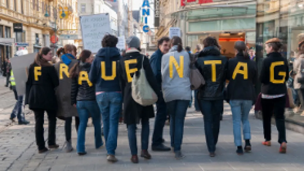 Menschen tragen Buchstaben auf Rücken, die "Frauentag" bilden. Straßenszene.