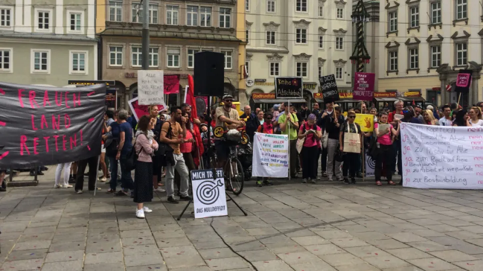Protestierende Menschenmenge mit Bannern auf einem Stadtplatz.