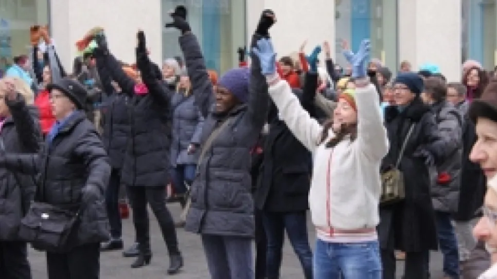 Menschen tanzen draußen, heben die Arme, bekleidet in Winterkleidung.