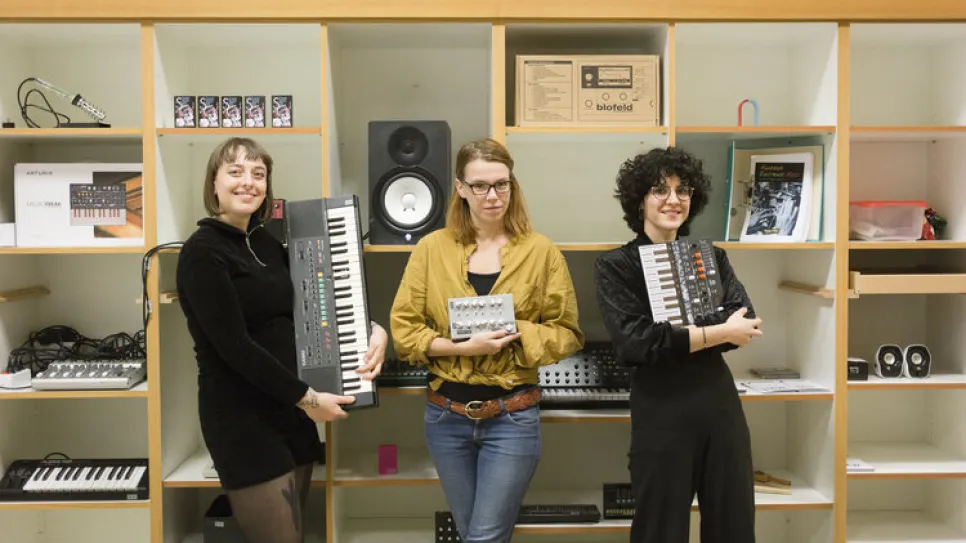 Drei Personen mit Keyboards in einem Musikraum.