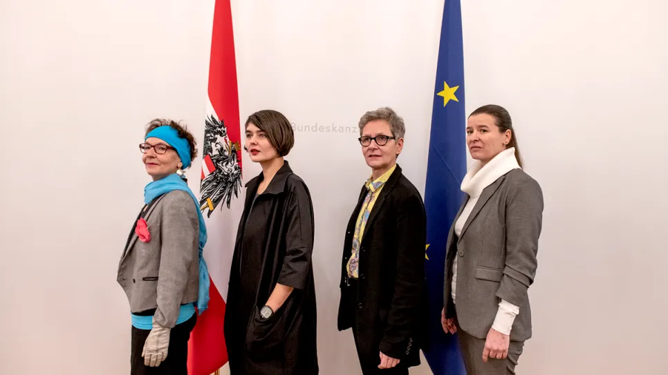 Vier Frauen in Business-Outfits, stehend vor österreichischer und EU-Flagge.