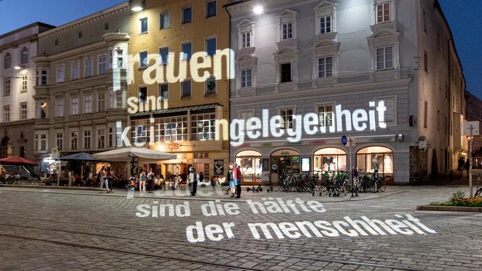 Beleuchtete Fassade mit Projektion auf Kopfsteinpflaster. Abendstimmung, Menschen im Hintergrund.