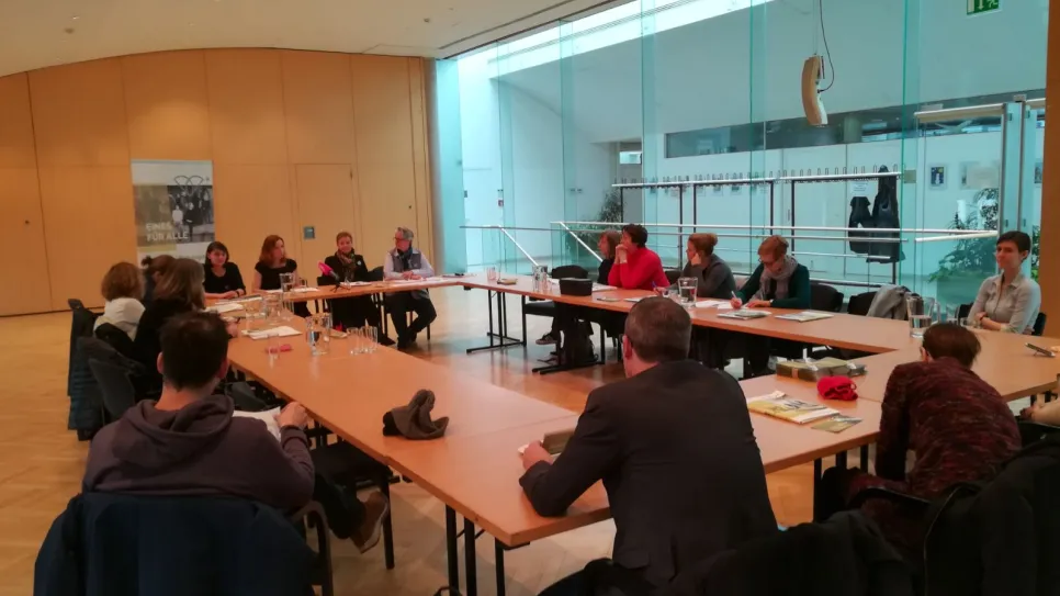Menschen in einer Besprechung sitzen an einem langen Tisch in einem modernen Raum.