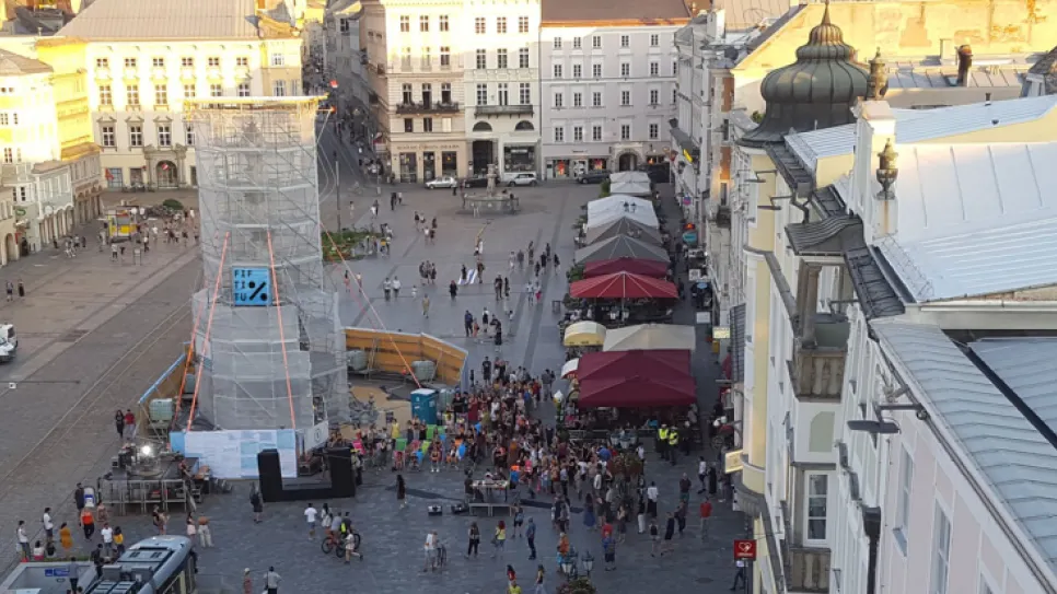 Stadtplatz mit Menschenmenge, Zelten und Bühne bei Sonnenuntergang.