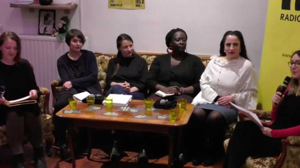 Diskussionsrunde mit sechs Frauen auf Sofas, Mikrofon und Tisch mit Getränken.