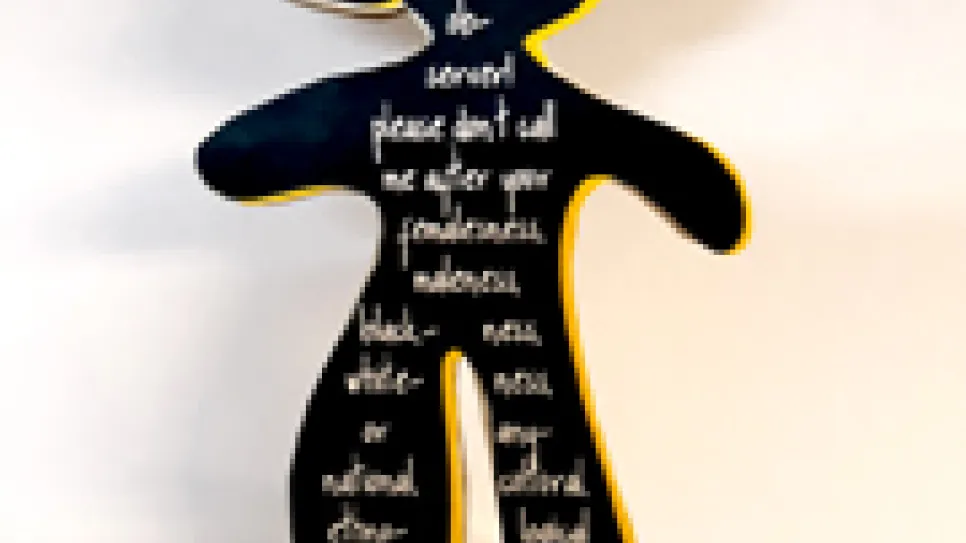 Schwarze Skulptur mit weißen Schriftzügen auf gelbem Sockel.