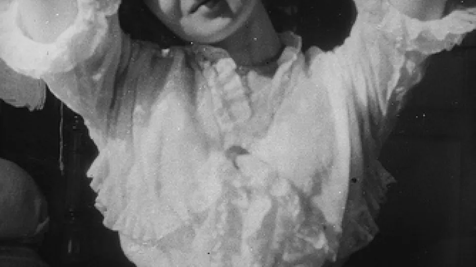 Junge Frau in weißer Bluse lächelt, Hände hinter dem Kopf. Schwarz-weiß-Fotografie.