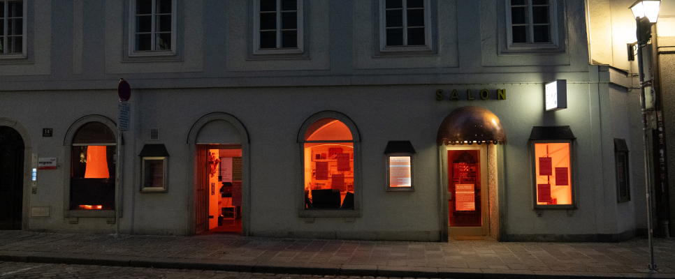 Eingang eines Gebäudes bei Nacht, Fenster leuchten orange.